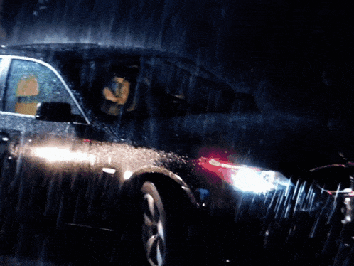a man driving a car in the rain with his headlights on