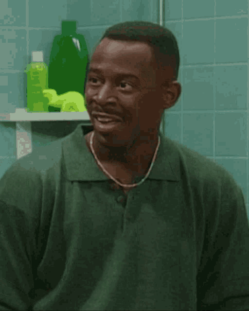 a man in a green shirt is laughing in front of a shelf with green bottles on it