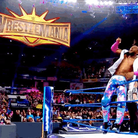 a wrestler in a ring with a wrestlemania sign above him
