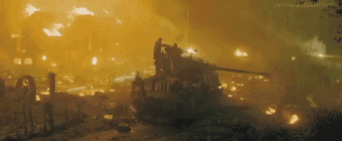 a group of people are standing on top of a tank in a burning city .