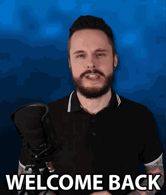 a man with a beard is standing in front of a microphone with the words welcome back written below him