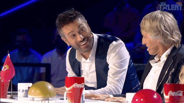 two men are sitting at a table with coca cola cups