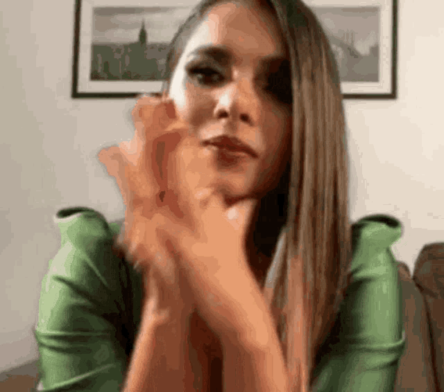 a woman in a green shirt is sitting on a couch with her hands folded and looking at the camera .