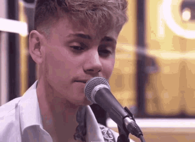 a young man singing into a microphone with a yellow light in the background