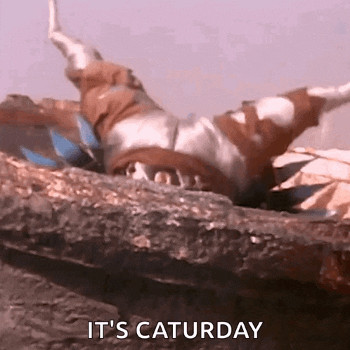 a power ranger is laying on his back on a rock with the words `` it 's saturday '' written below him .
