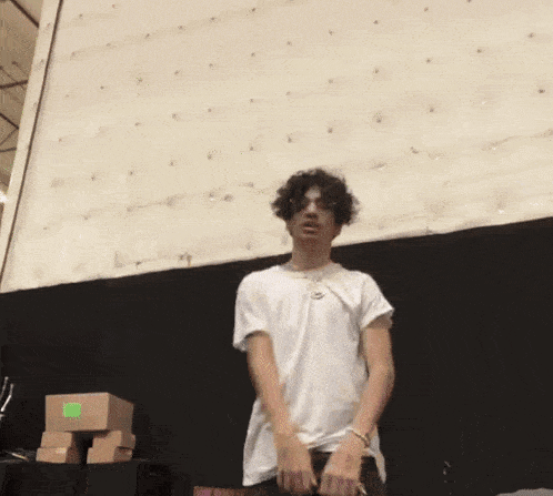 a young man in a white shirt is standing in front of a wall with boxes on it