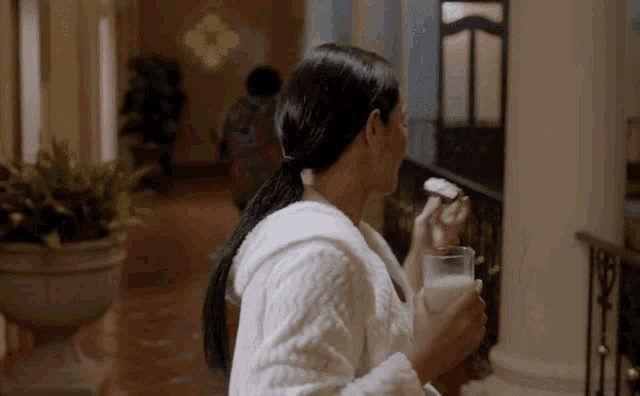a woman in a bathrobe holds a glass of milk and a piece of cake