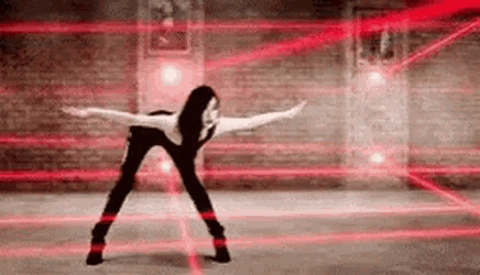 a woman is dancing in a room with red lasers coming out of the walls .