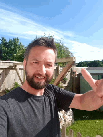a man with a beard wearing a black shirt is giving a thumbs up