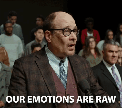 a man in a suit and tie is speaking into a microphone with the words " our emotions are raw " behind him