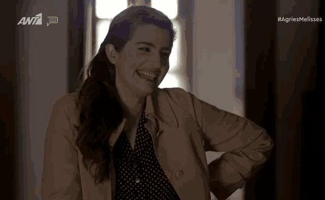 a woman in a trench coat is smiling in front of a screen that says ant7