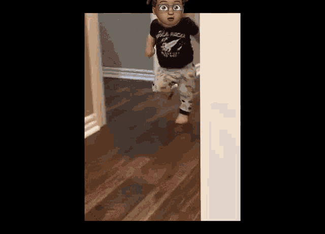 a little boy wearing glasses and a black shirt is standing on a wooden floor .