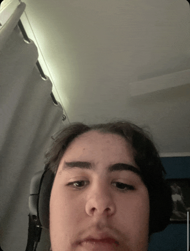 a young man wearing headphones looks at the camera with his eyes closed