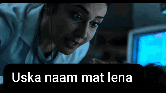 a woman looking at a computer screen with the words uska naam mat lena