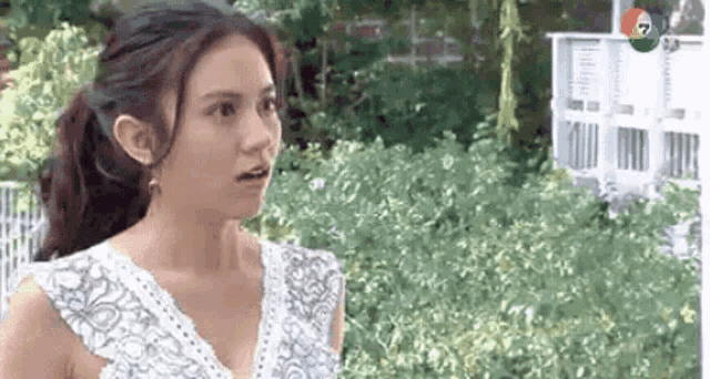 a woman in a white dress is standing in front of a house and talking to someone .