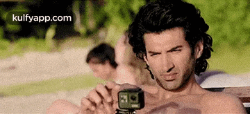 a man without a shirt is taking a selfie with a camera .