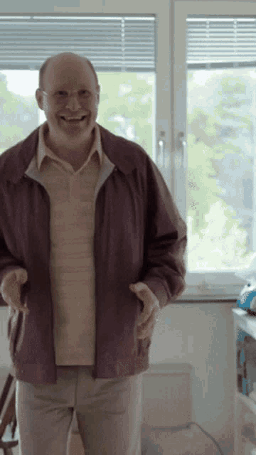 a man in a purple jacket stands in front of a window smiling