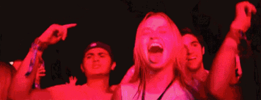 a group of people are dancing at a concert with their arms in the air .
