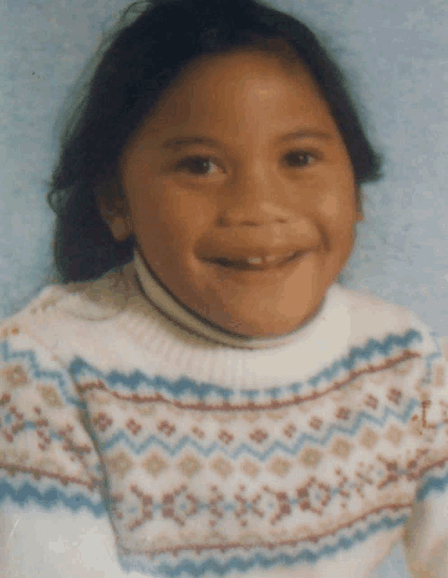 a young girl wearing a sweater with a geometric pattern smiles for the camera
