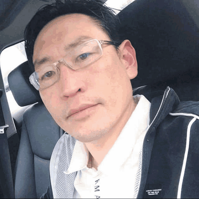 a man wearing glasses is sitting in a car and his shirt says kma