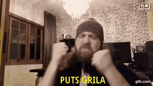 a man with a beard wearing a beanie is making a funny face in a living room .