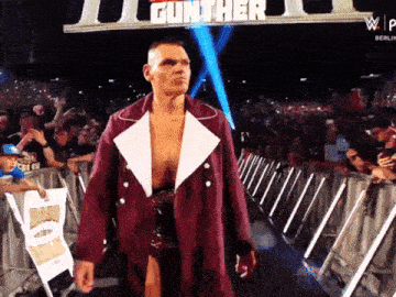 a man in a maroon coat walks into a wrestling ring with gunther written on the screen behind him