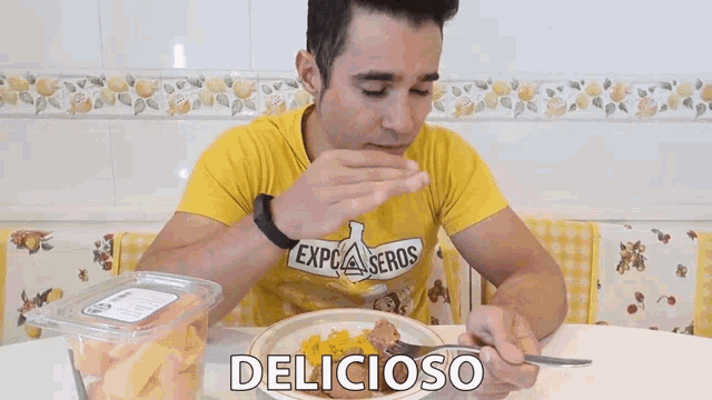 a man in a yellow shirt is eating a plate of food with the word delicioso written on the table