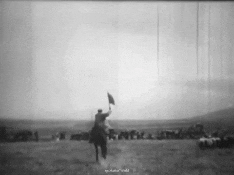 a black and white photo of a man on a horse holding a flag in a field .