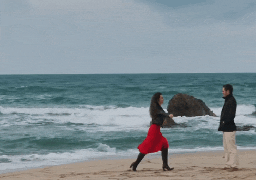 a man and a woman dancing on a beach near the ocean