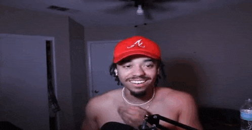 a shirtless man wearing a red hat with the letter a on it is standing in front of a microphone .