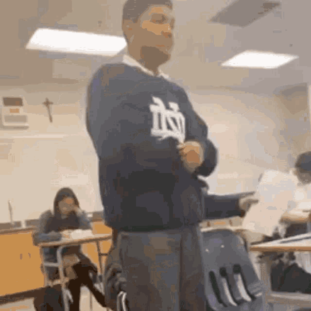 a man in a sweater with the letter n on it is standing in a classroom .