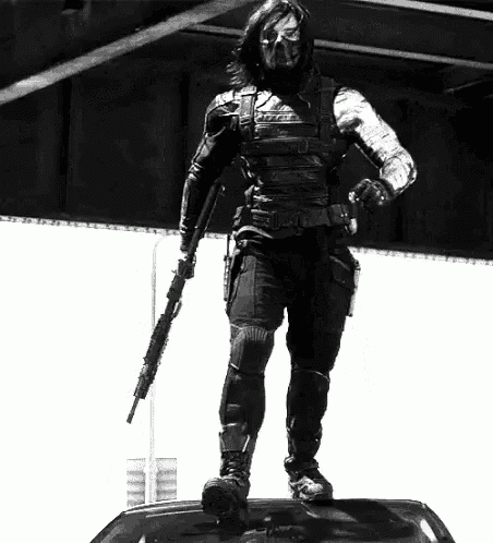 a black and white photo of a man standing on top of a car holding a rifle .