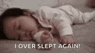 a baby is sleeping on a bed with the words `` i over slept again '' above it .