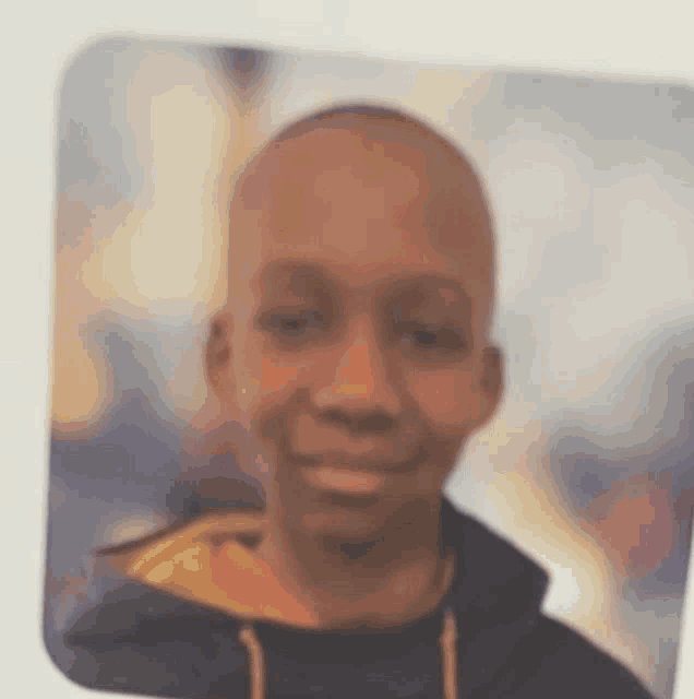 a young man with a shaved head is smiling for the camera in a blurry photo