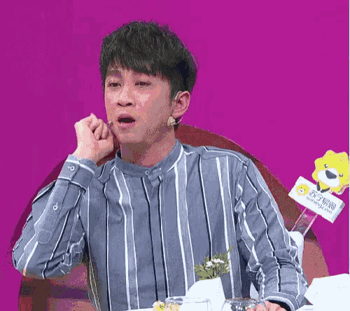a man in a striped shirt is sitting at a table with a purple background .