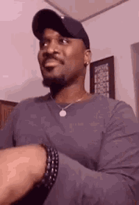 a man wearing a hat and a necklace is smiling while looking at his watch .