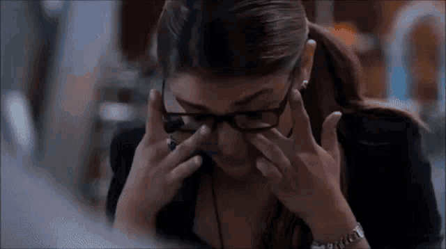 a woman wearing glasses is rubbing her eyes with her hands while sitting at a desk .