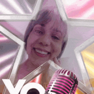 a woman is smiling in front of a pink star and a microphone