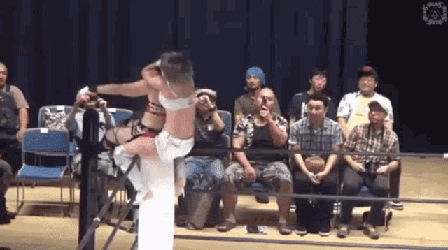 a group of people are watching a wrestling match and one of the wrestlers is wearing a white bra
