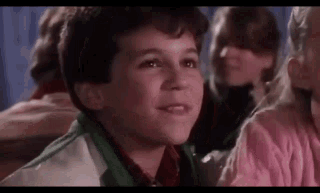 a young boy in a green and white jacket is sitting in a crowd of people .