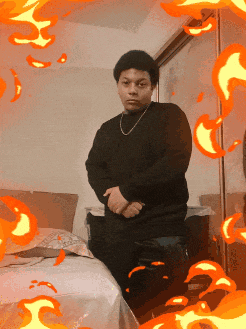 a man in a black sweater is standing in front of a bed with flames surrounding him