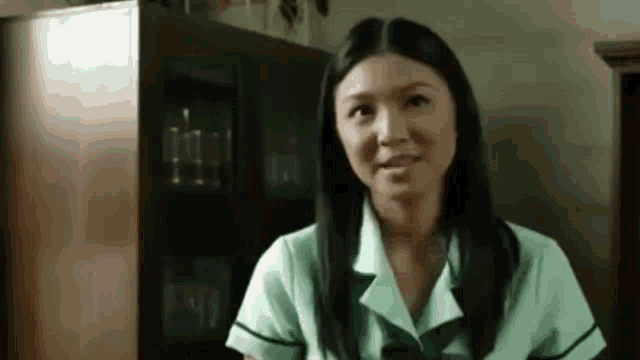 a woman in a green uniform is standing in a room and smiling .