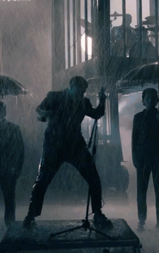 a man singing into a microphone in the rain with umbrellas
