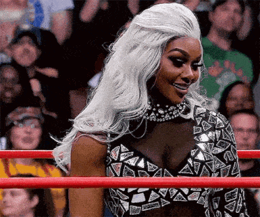 a woman with long white hair is standing in a wrestling ring .