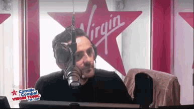 a man talking into a microphone in front of a virgin sign