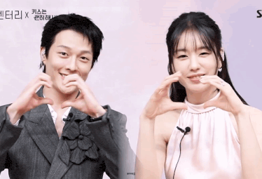 a man in a suit and a woman in a pink dress are making a heart shape with their hands