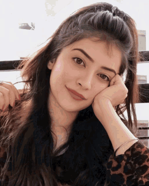 a woman rests her head on her hand while wearing a leopard print shirt