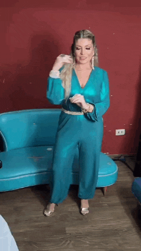 a woman in a blue jumpsuit is standing in front of a blue couch and dancing .