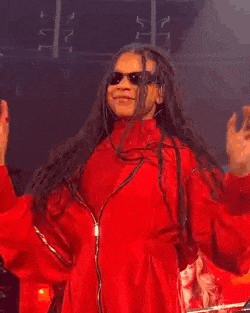 a man with dreadlocks is wearing a red jacket and sunglasses and dancing on a stage .