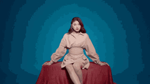 a woman in a tan dress is sitting on a red couch with her legs crossed .